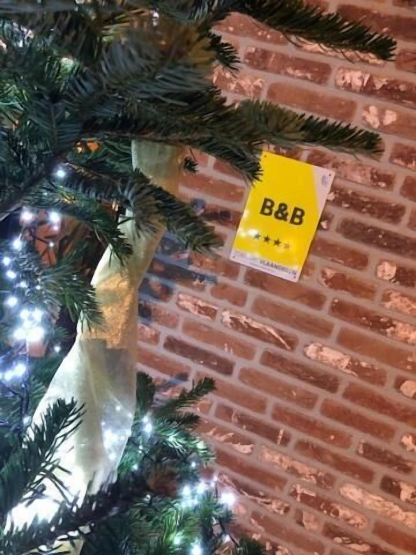 Un muro de ladrillo con un árbol de Navidad y un letrero amarillo que dice "B&B" y muestra tres estrellas.