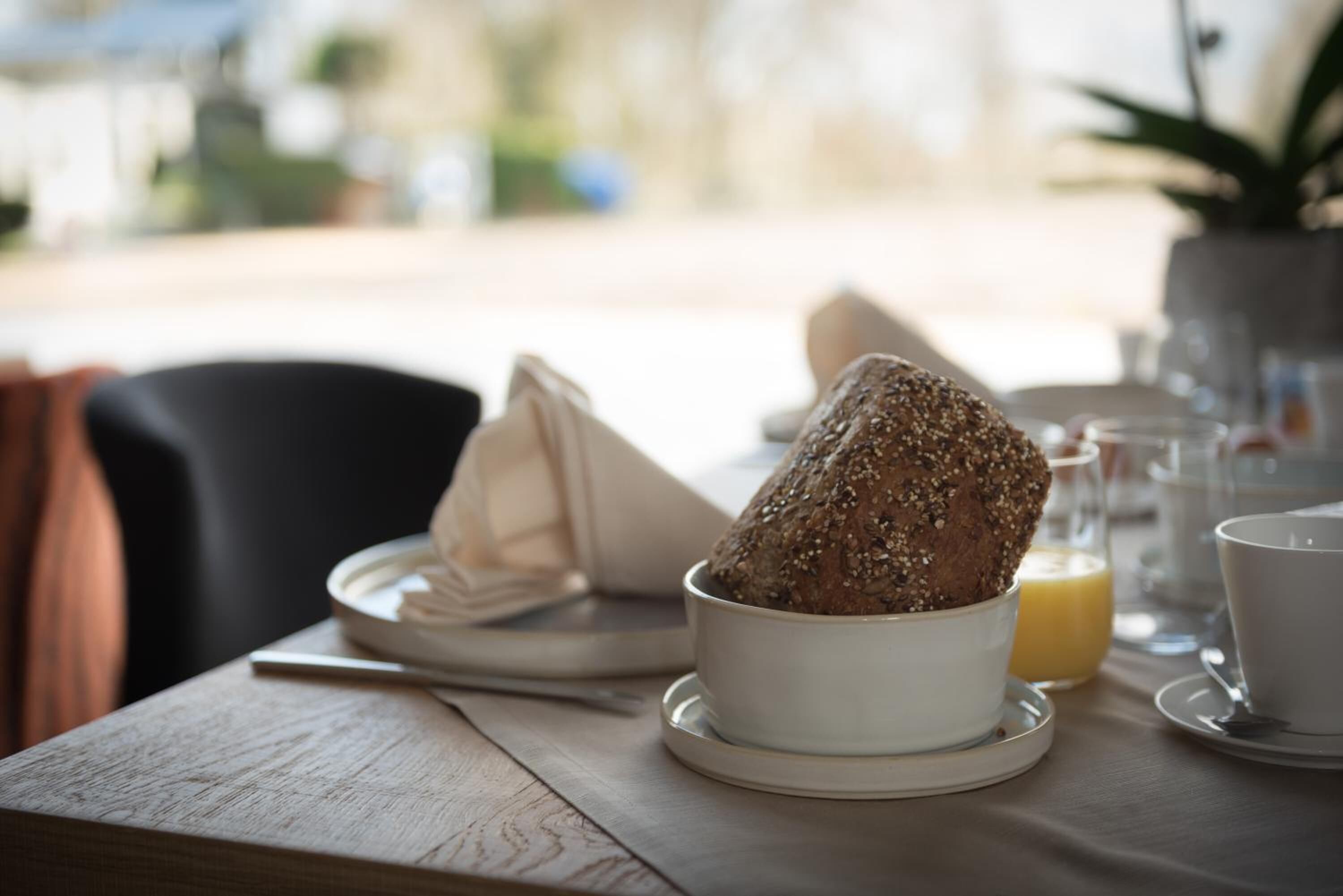 En morgenmadsopsætning med en skål brød, en serviet, et glas appelsinjuice og en kop på et træbord.