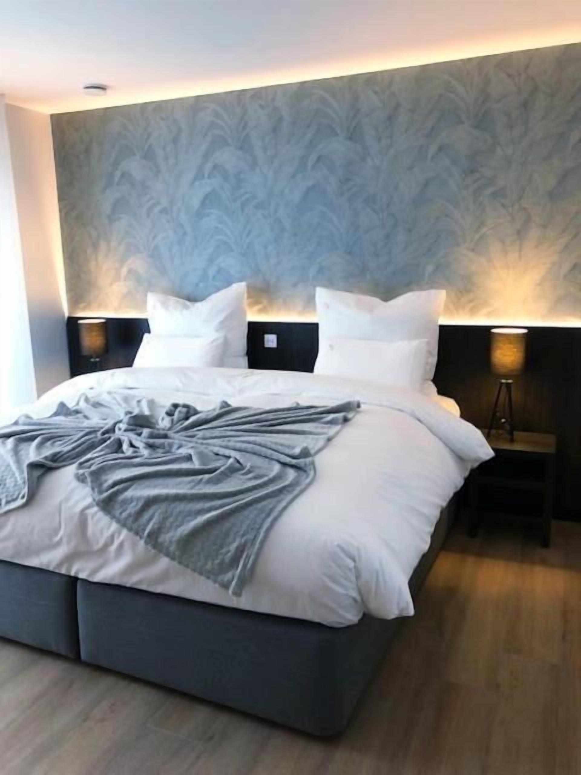 A modern bedroom with a large bed, two bedside tables with lamps, and a patterned wall.