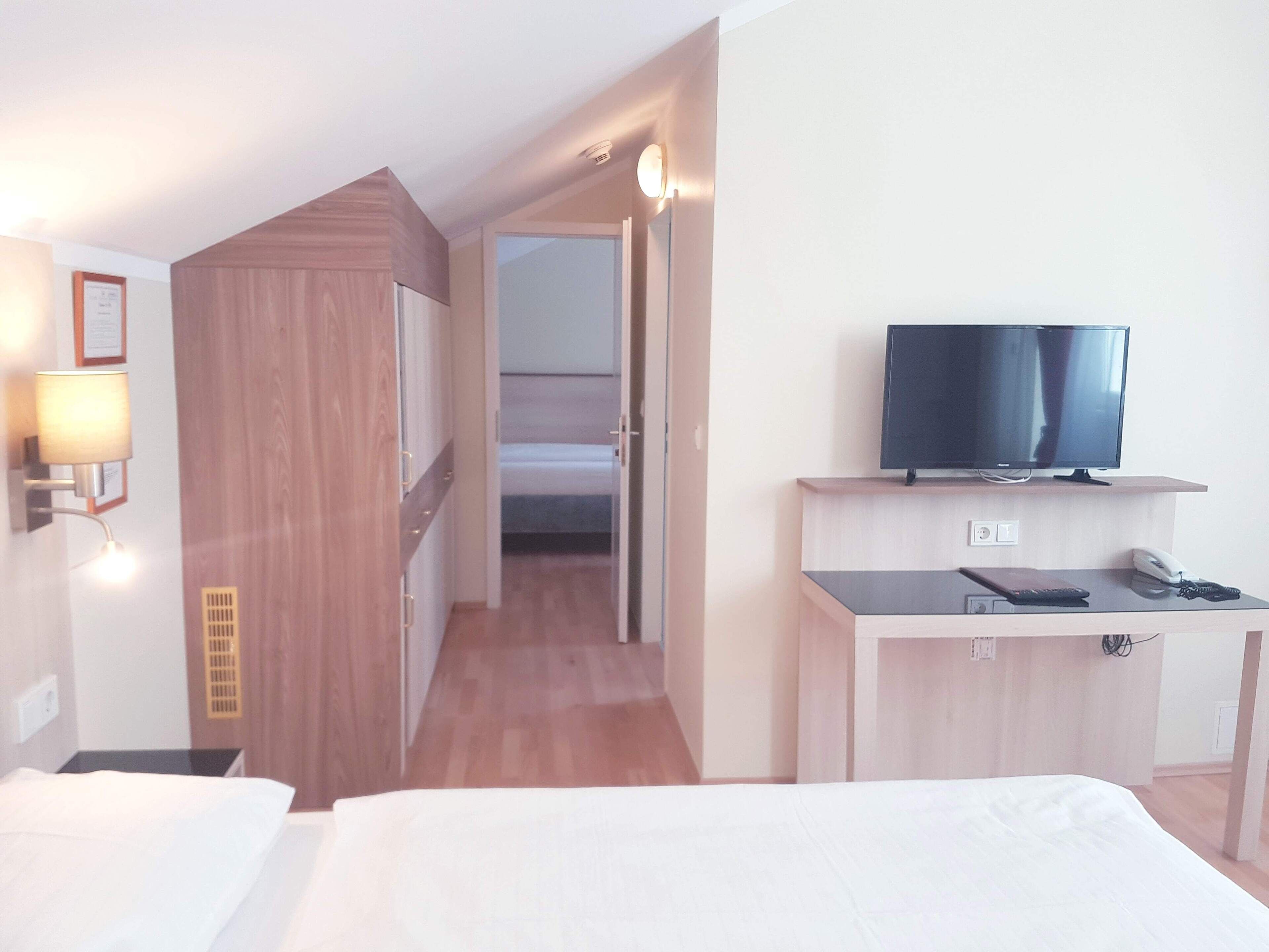 Una habitación de hotel con una cama, un escritorio con televisor, teléfono y lámpara.