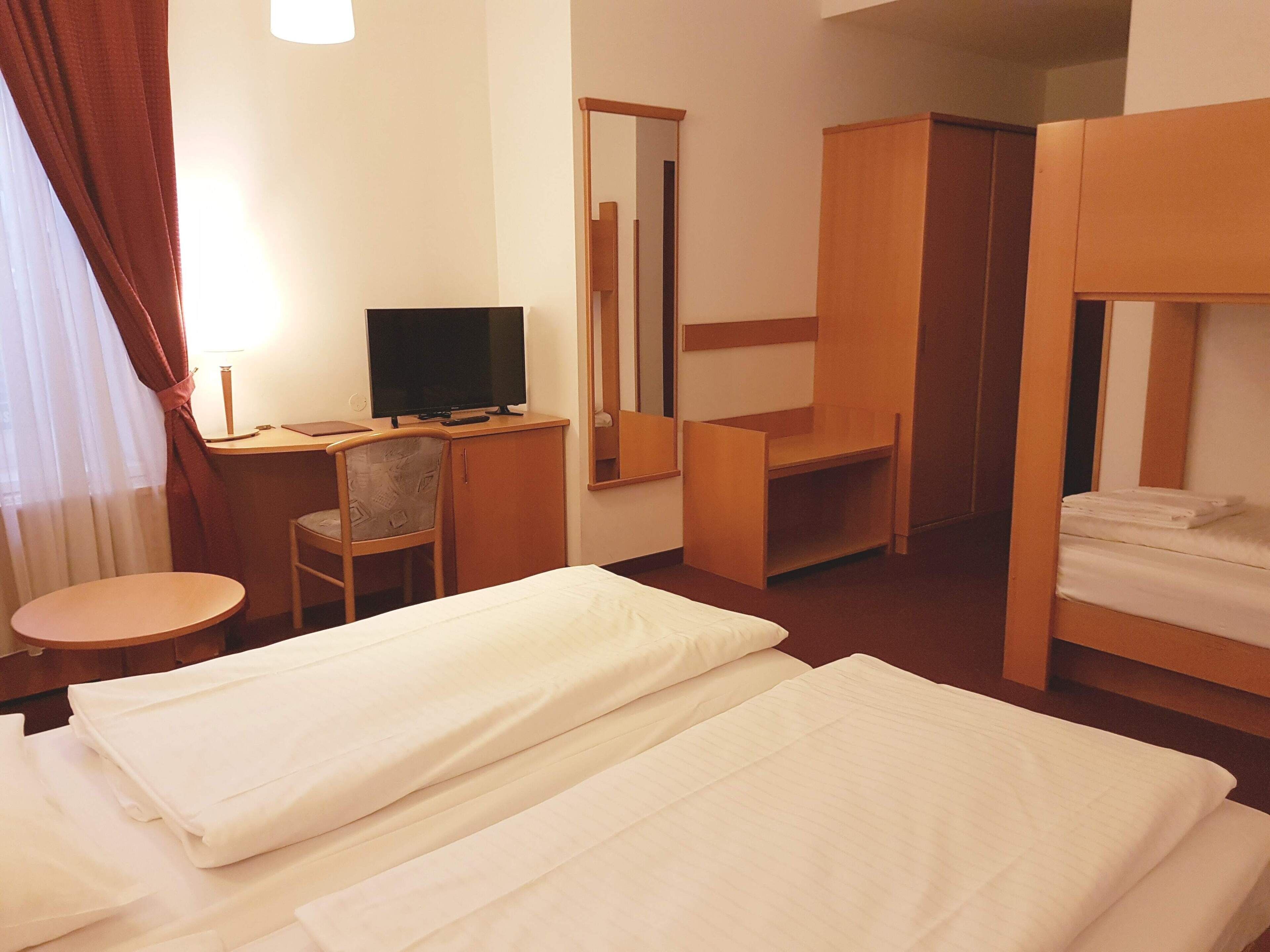 Habitación de hotel con dos camas, un escritorio con televisor, una silla y un espejo.