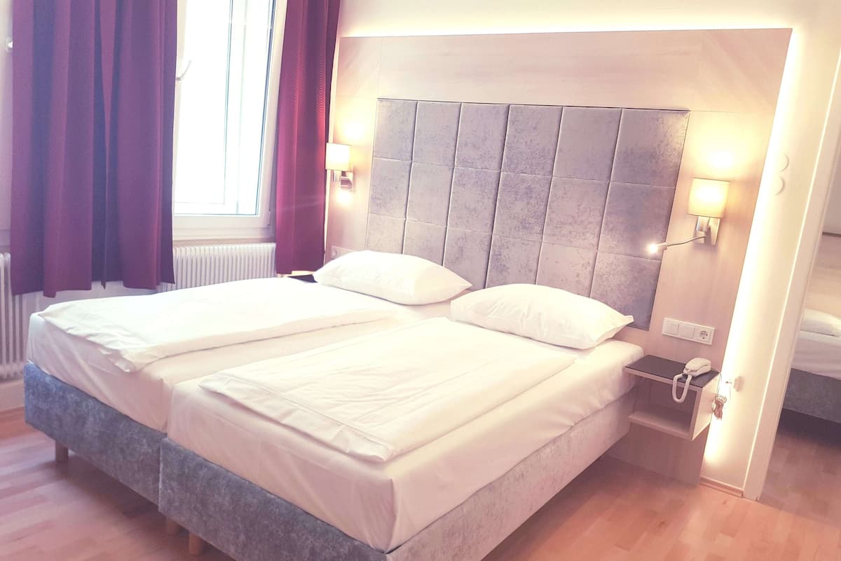 Un lit double avec une tête de lit grise, du linge de lit blanc et deux lampes de chevet.