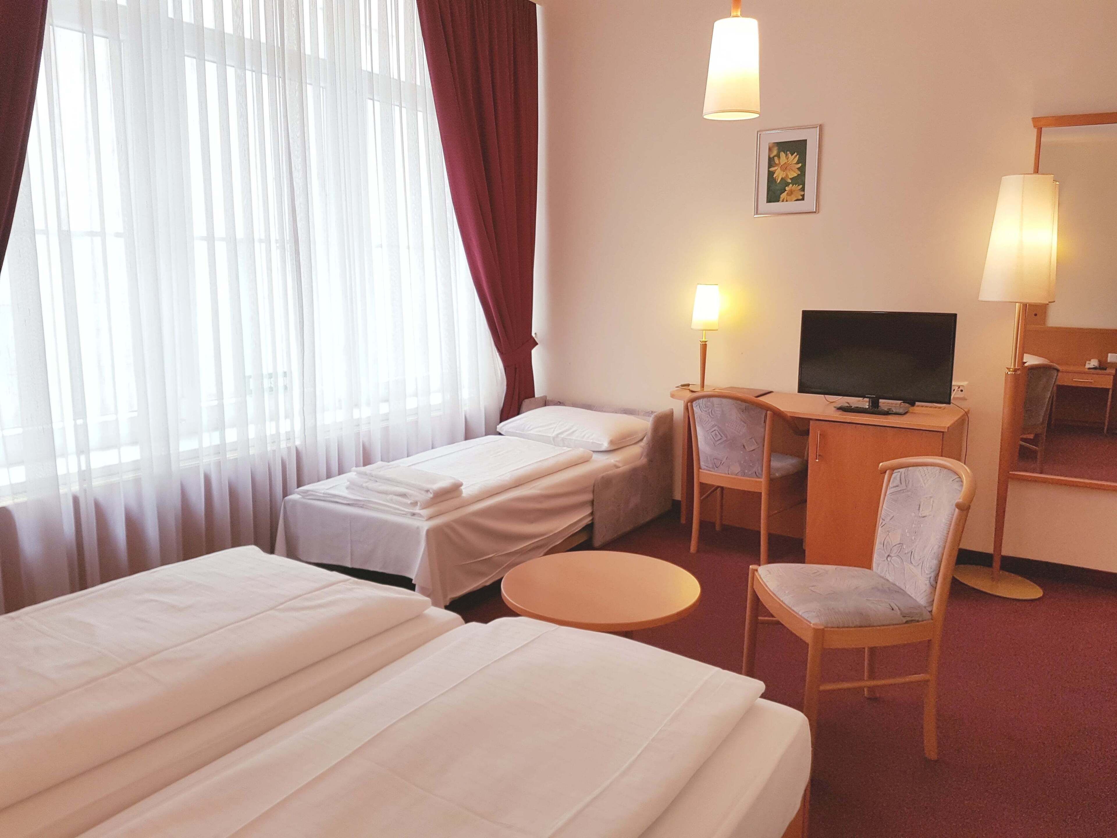 Habitación de hotel con dos camas, un escritorio con televisor, una silla y una mesita.