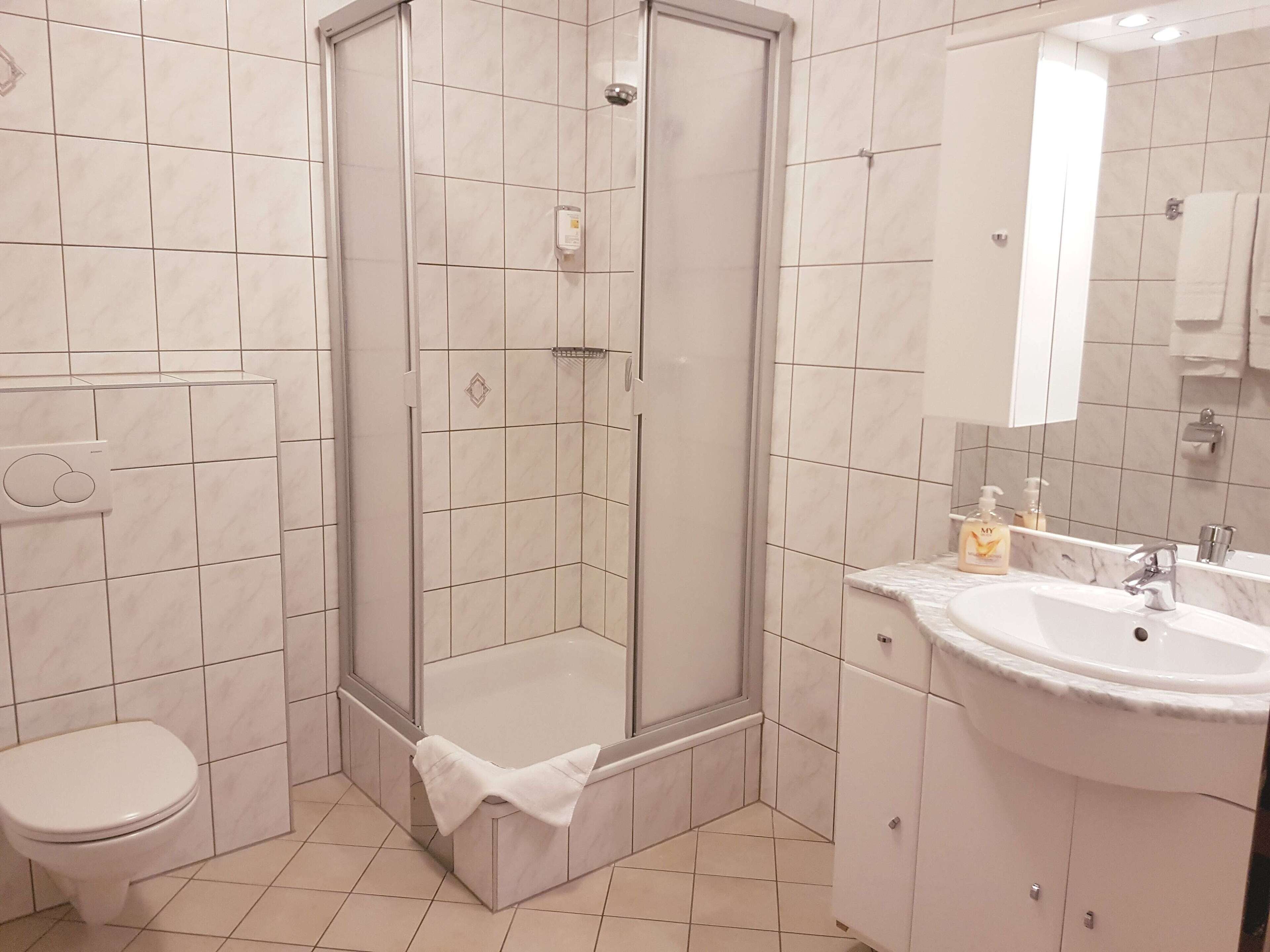 Un baño moderno con ducha acristalada, inodoro y lavamanos con espejo.