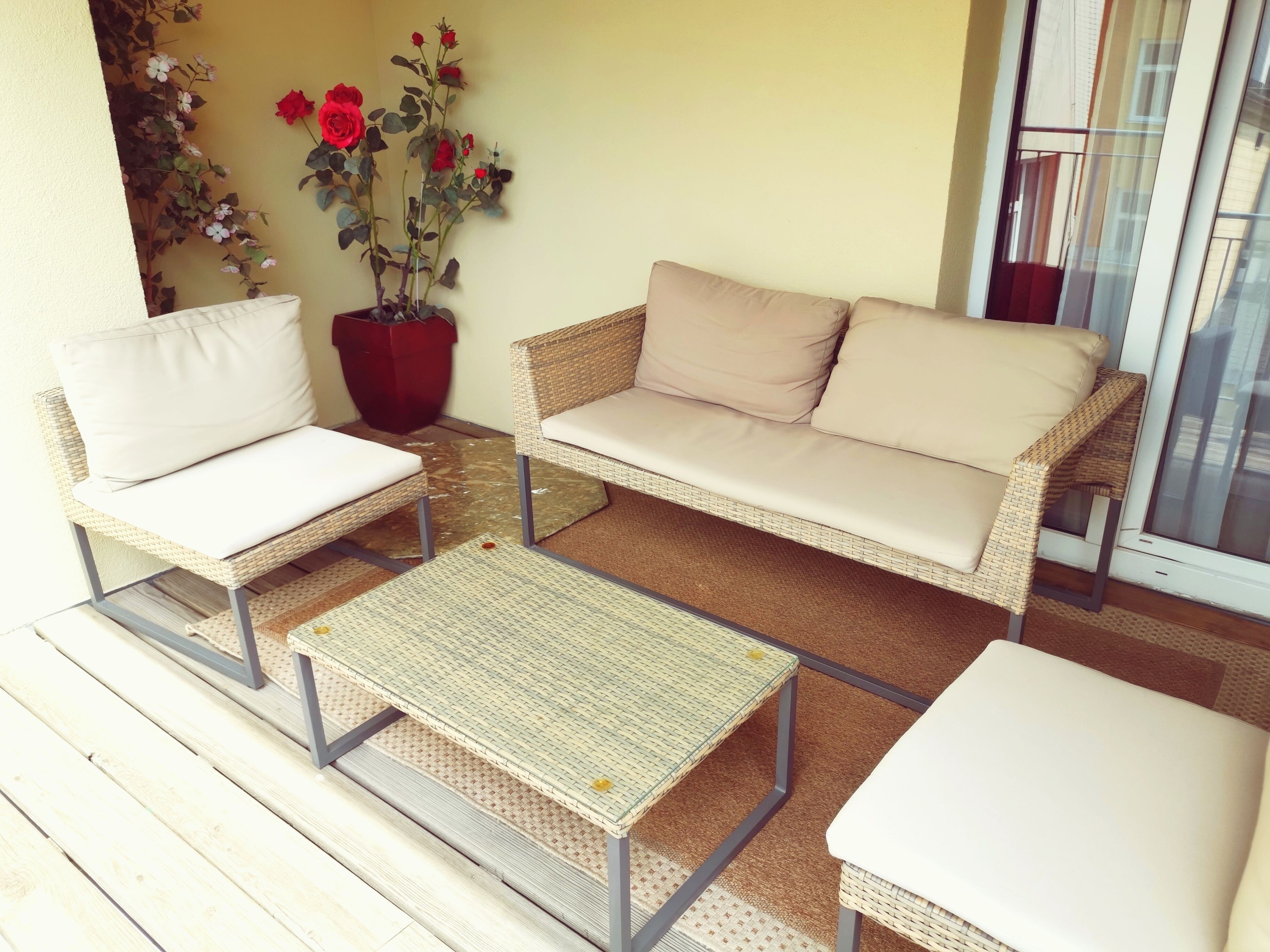 Un patio con mobiliario de mimbre, incluyendo dos sillas, un sofá, una mesita y una maceta con flores.
