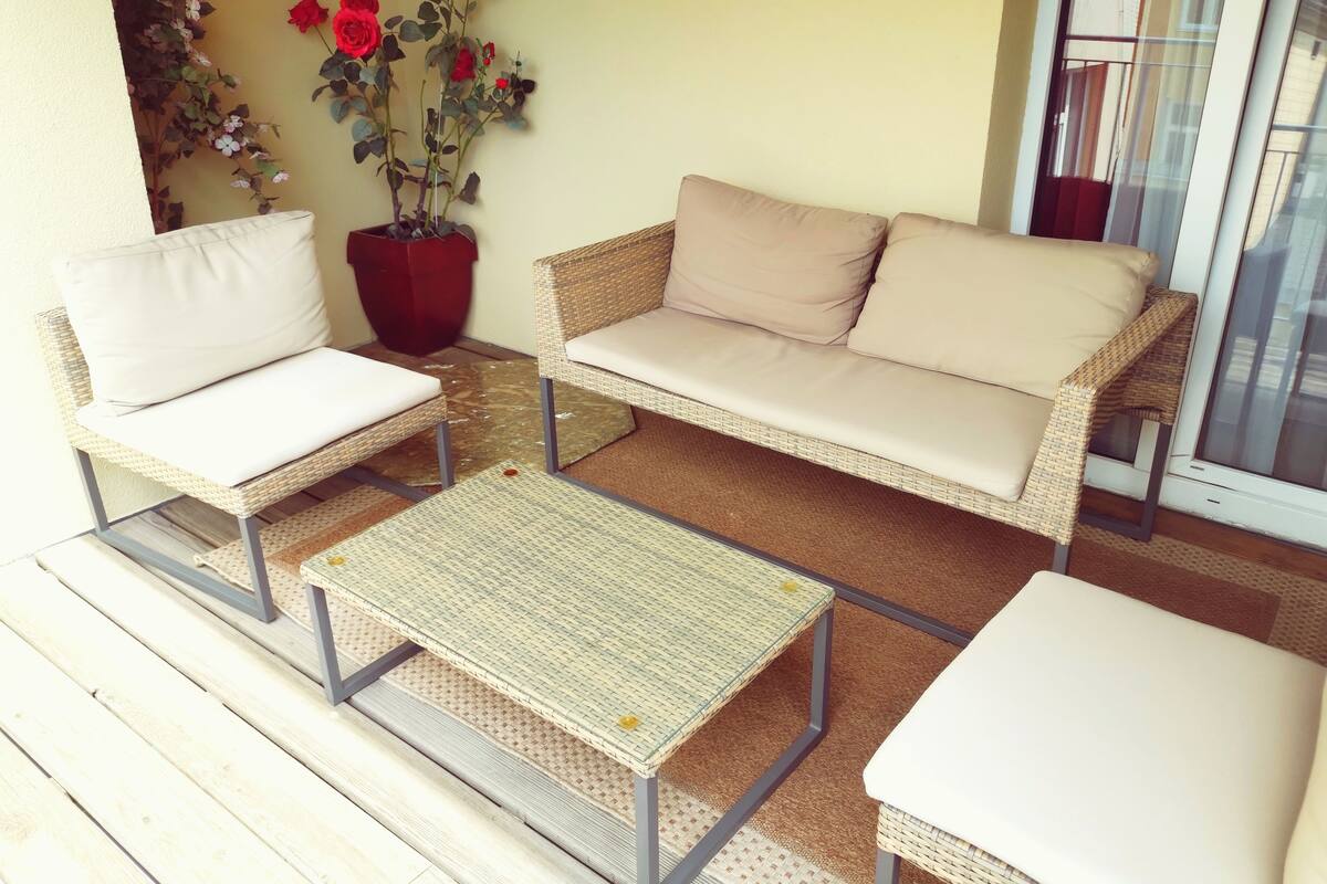 Un espace patio aménagé avec des meubles en osier, comprenant deux chaises et un canapé, une petite table et un pot de fleurs.