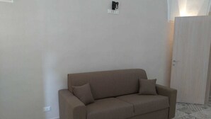 Un sofá color beige en una habitación con baldosas de piso estampadas y una puerta de color claro.
