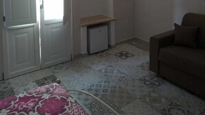 Una habitación con una puerta blanca, un mueble blanco pequeño, un sofá marrón y una alfombra estampada.