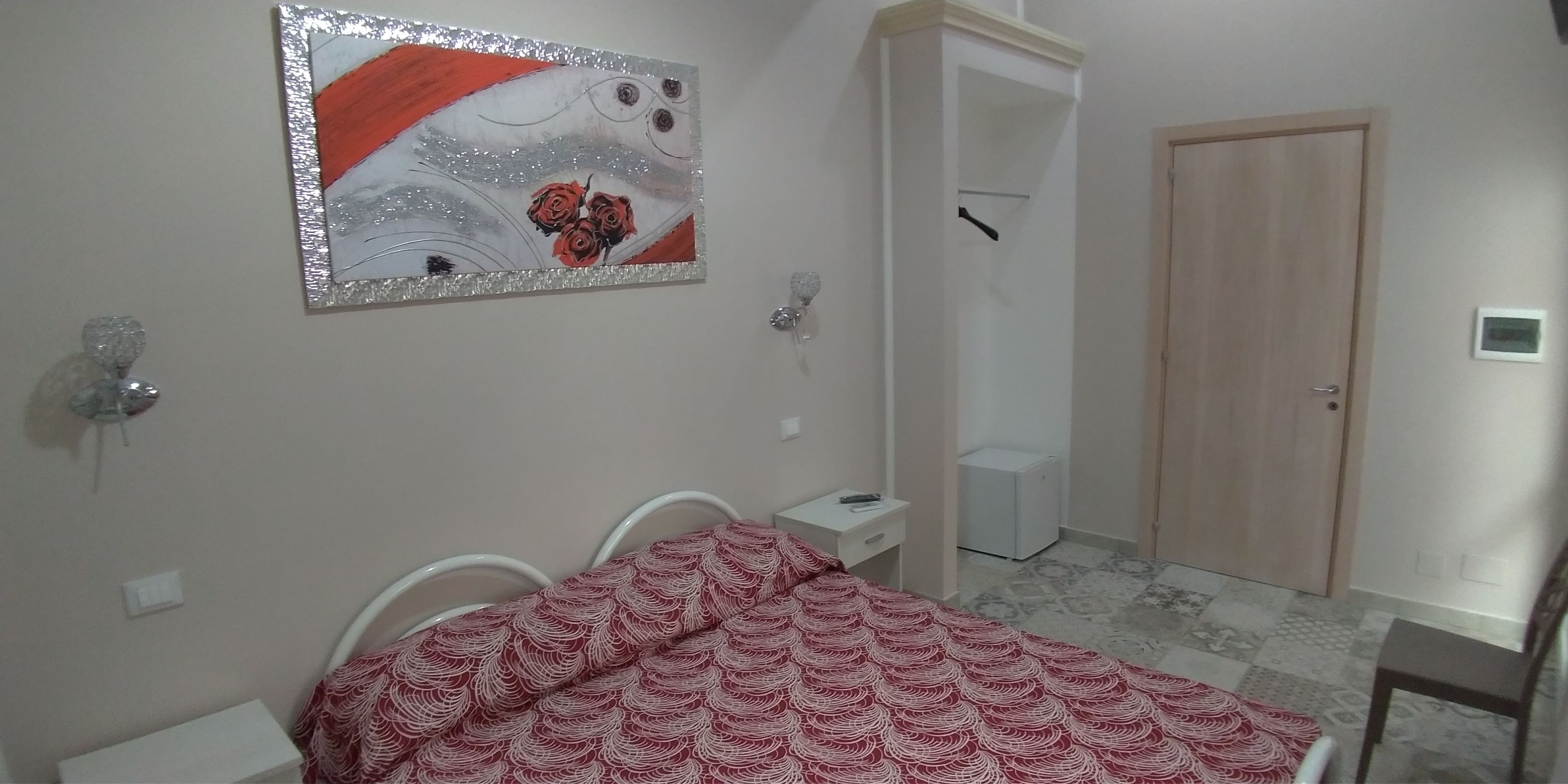 Une chambre à coucher comprenant un lit, une table de chevet, une lampe fixée au mur, une porte et une petite armoire blanche.