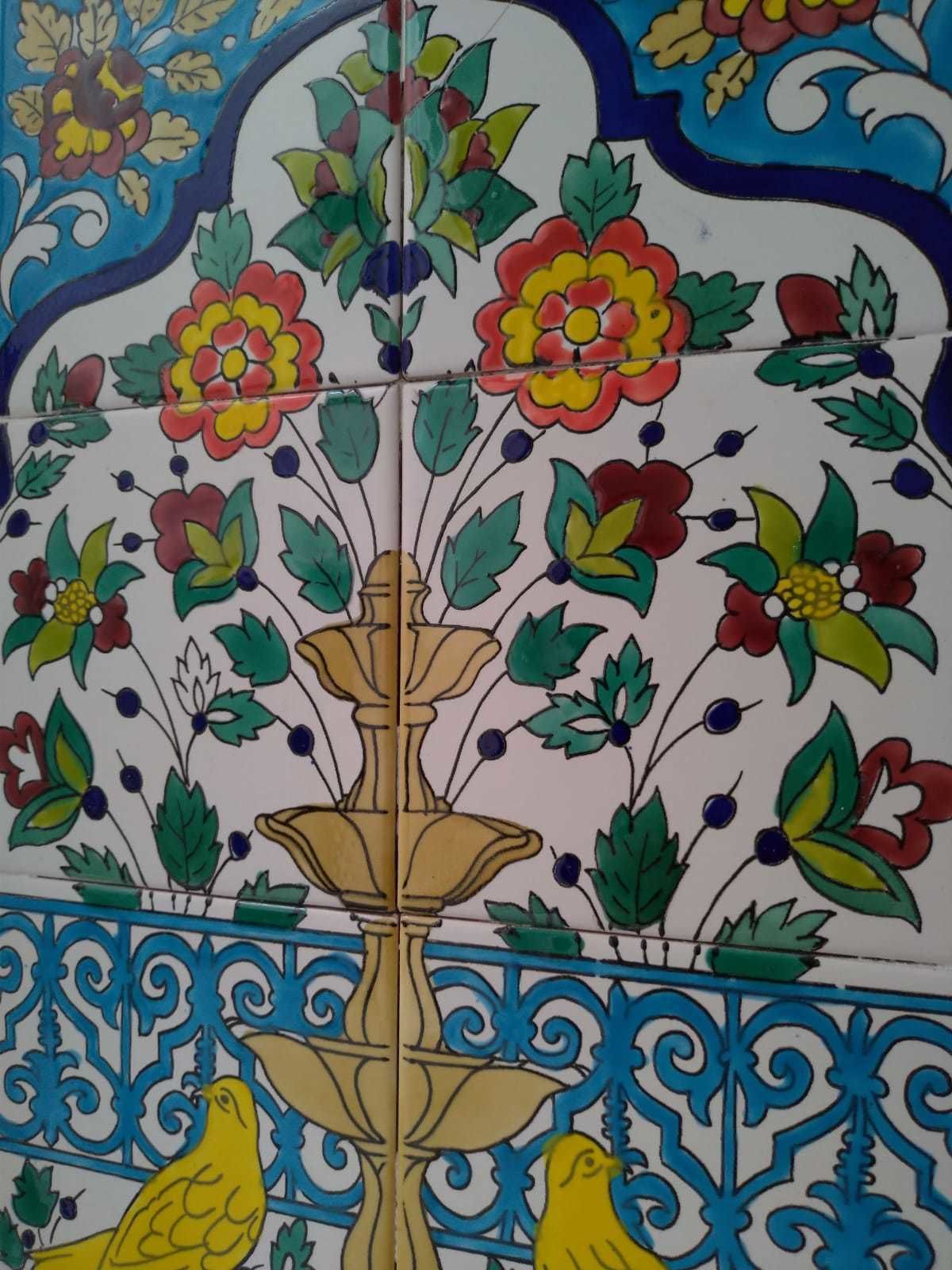 Eine mit Fliesen verkleidete Wand mit einem floralen Muster, einem zentralen Brunnenmotiv und zwei gelben Vögeln im unteren Bereich.