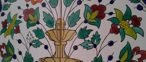 Eine mit Fliesen verkleidete Wand mit einem floralen Muster, einem zentralen Brunnenmotiv und zwei gelben Vögeln im unteren Bereich.