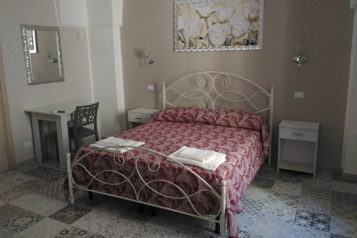 A bedroom with a bed, bedside tables, a desk, a chair, and a mirror.
