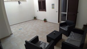 Un pequeño patio con mobiliario de mimbre, suelo de baldosas y una puerta que da a un balcón.