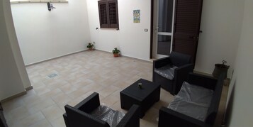 Um pequeno espaço ao ar livre com móveis de vime, piso de azulejos e uma porta que dá para uma varanda.