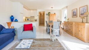 A modern living room with a sofa, a coffee table, and a dining area with chairs and a table. - Monet (Koksijde)