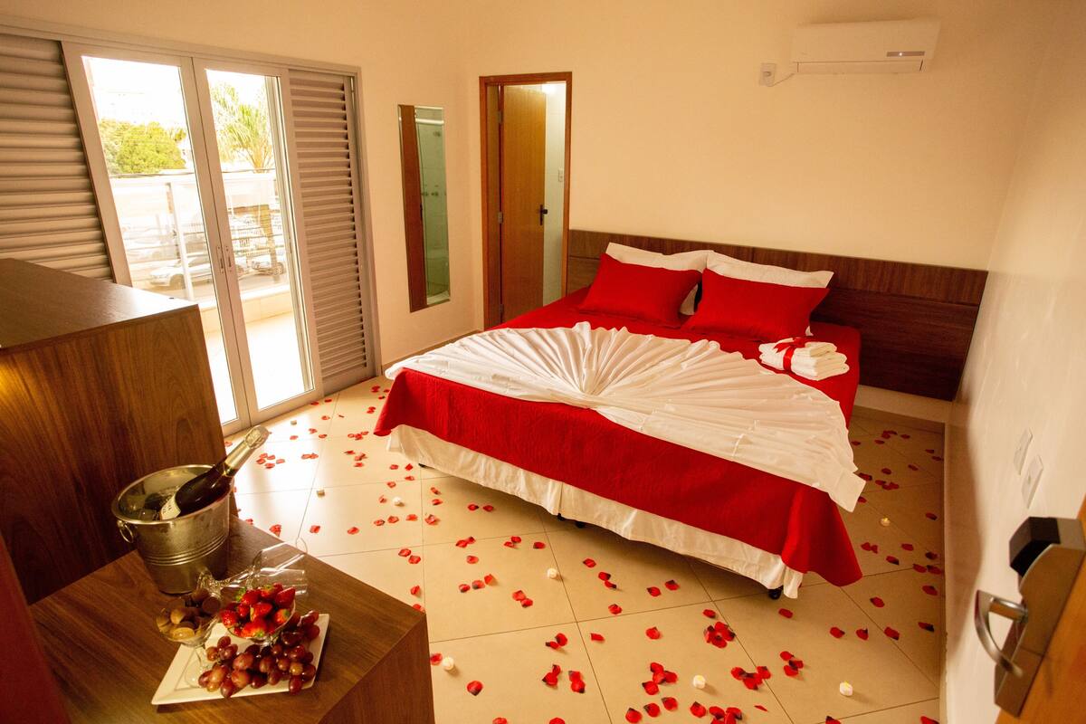 Habitación de hotel con una cama, un cubo con una botella, una bandeja con frutas y una puerta que da a un balcón.