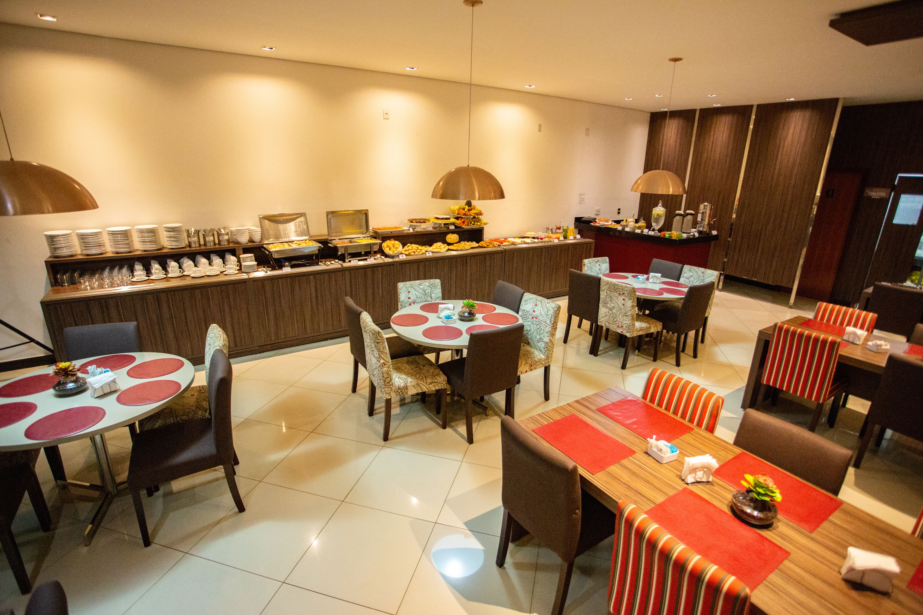 A hotel dining area with multiple round tables, chairs, and a buffet counter.