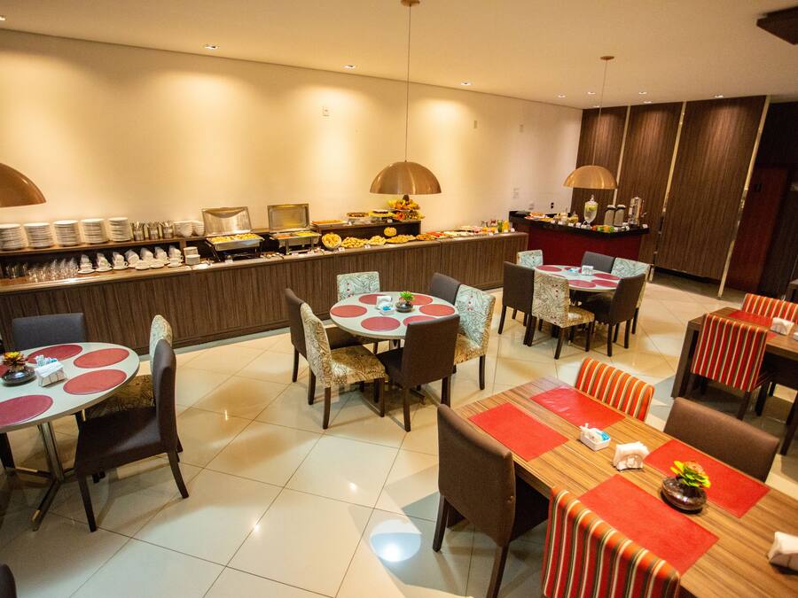 Un comedor de hotel con varias mesas redondas, sillas y una barra de buffet.