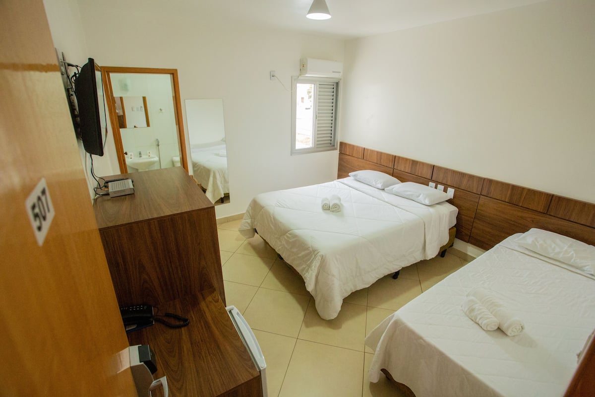 Una habitación de hotel con dos camas, un escritorio con computadora, un espejo y una ventana con persianas.