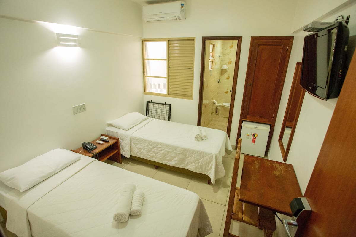 Habitación de hotel con dos camas, una mesita, televisor y ventana con persianas.