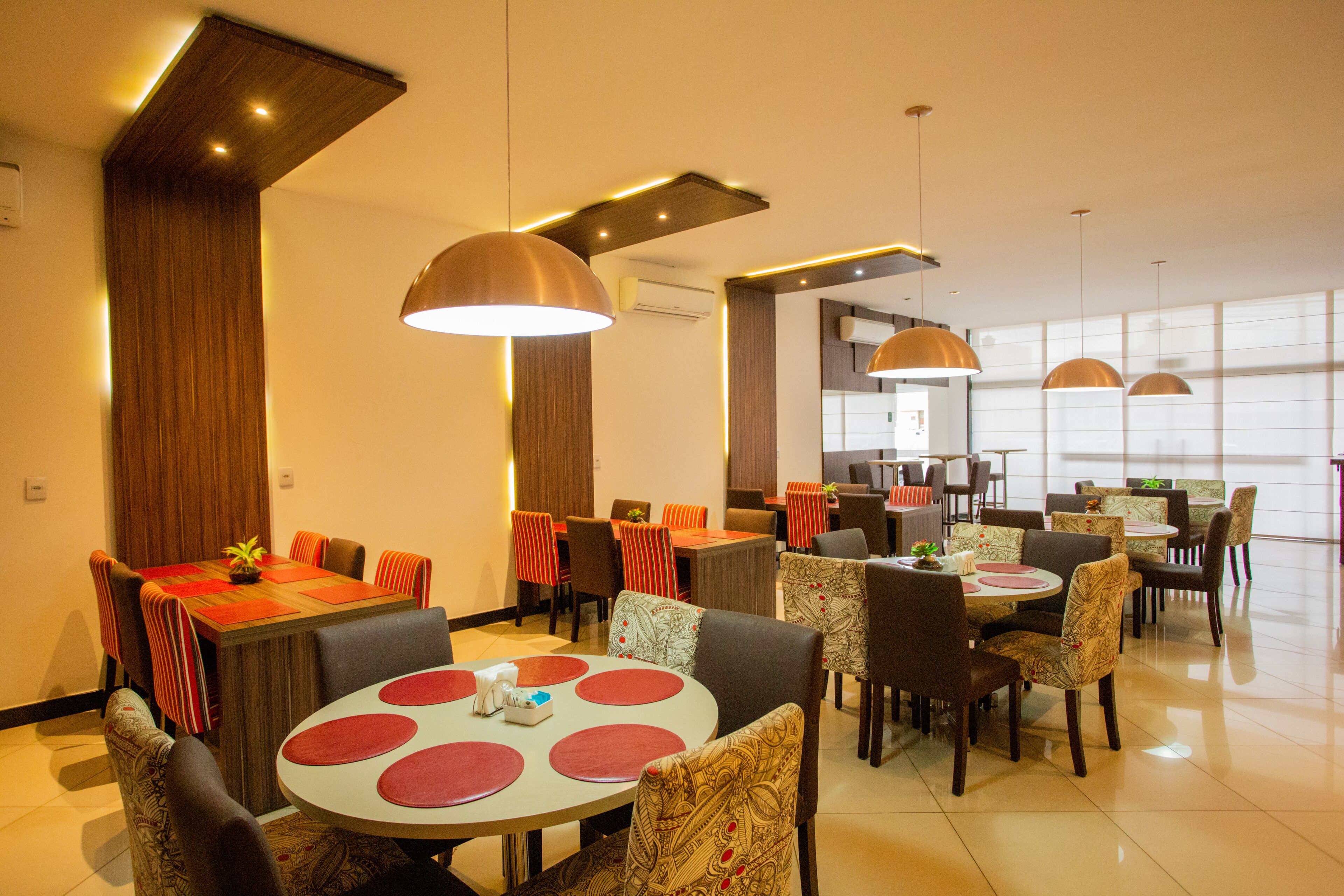 A modern dining area with multiple tables and chairs, wooden accents, and pendant lighting.