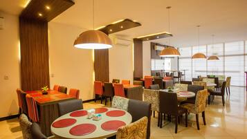 A modern dining area with multiple tables and chairs, wooden accents, and pendant lighting.