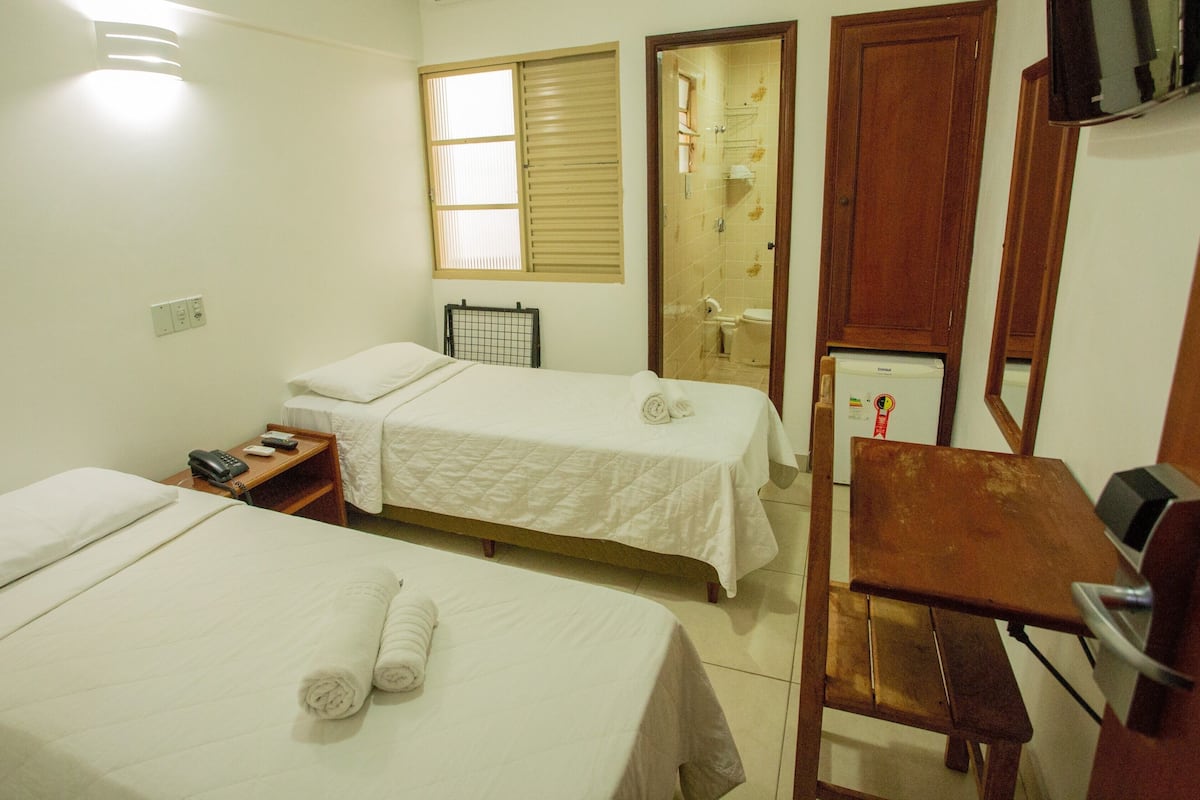 Habitación de hotel con dos camas, un escritorio, una silla, un refrigerador y un televisor.
