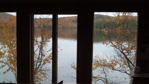 Una habitación con un ventanal grande que da a un lago rodeado de árboles otoñales.