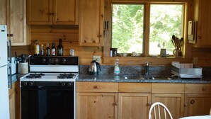 Una cocina con armarios de madera, estufa y ventana con vista a árboles.