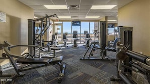 A gym with various exercise equipment, a carpeted floor, and large windows offering a view.