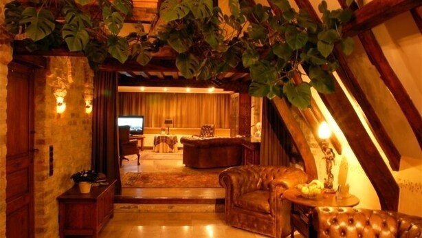 Ein gemütlicher, rustikaler Raum mit freiliegenden Holzbalken, einem Ledersofa, einem Holztisch und einem Fernseher im Hintergrund.