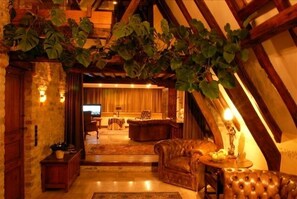 Una habitación acogedora y rústica con vigas de madera a la vista, un sofá de cuero, una mesita de centro de madera y un televisor al fondo.