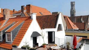 Eine Dachterrasse mit einem weißen Gebäude, roten Ziegeldächern und einem Kirchturm im Hintergrund.