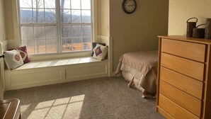 A bedroom with a large window, a wooden dresser, and a wall clock.