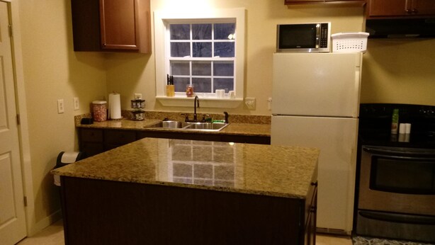 A kitchen with granite countertops, a stainless steel refrigerator, a microwave, and a window above the sink.