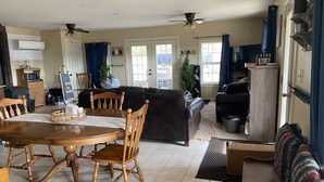 A spacious living room with a dining area, featuring a wooden dining table, chairs, a sofa, and a television.