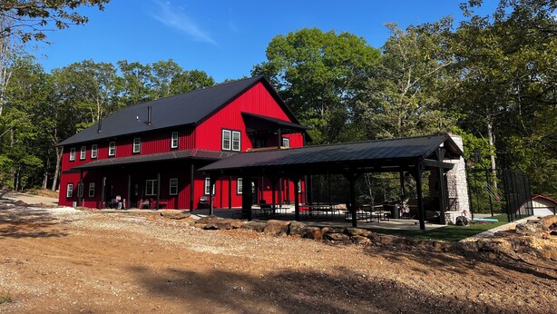A red barn with a black roof, surrounded by trees and a dirt path. - Family Cabin with a large front porch - Close to playground and pond (Winslow)