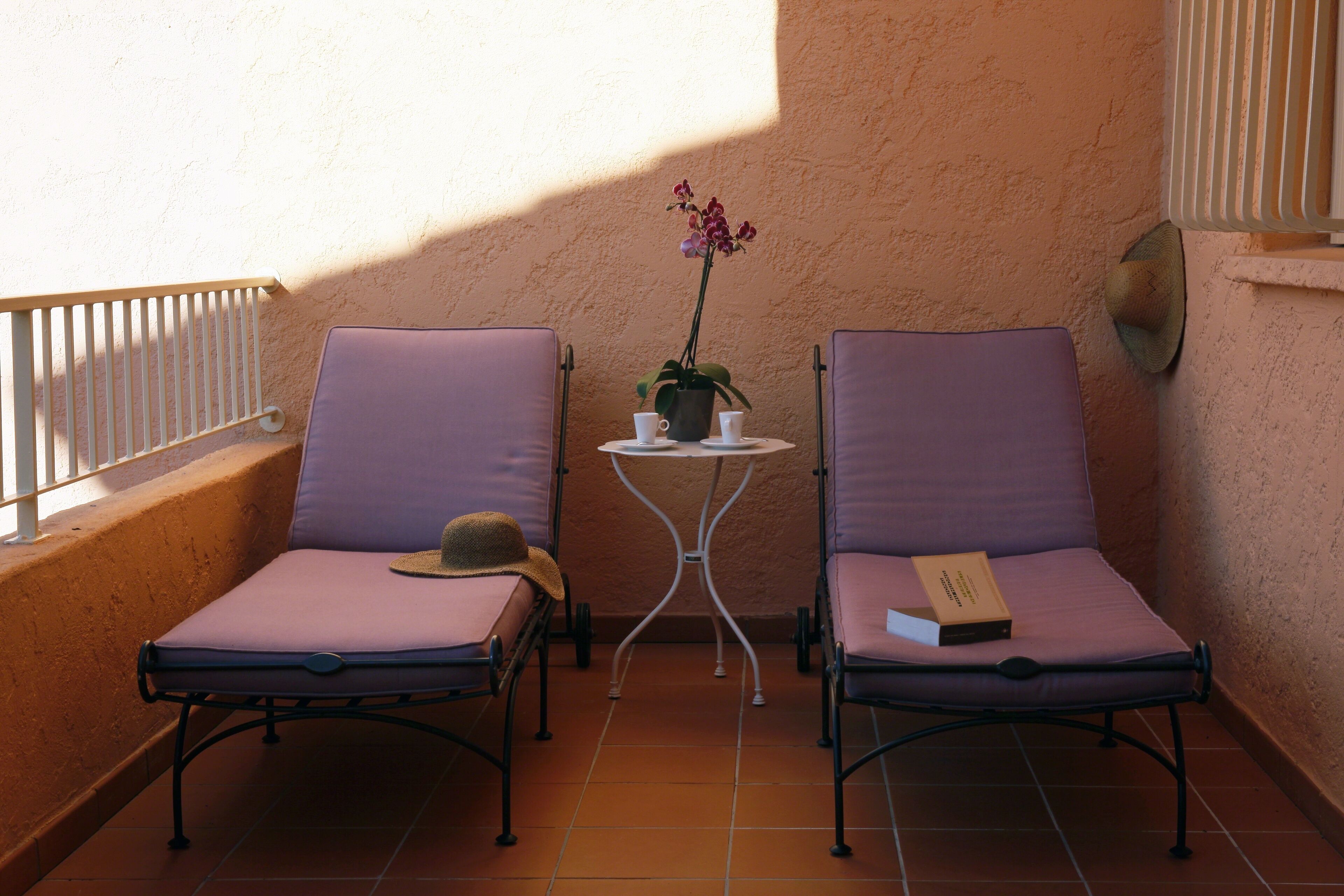 Twee paarse fauteuils met metalen poten, een kleine ronde tafel met een bloeiende orchidee en een boek op één van de stoelen.
