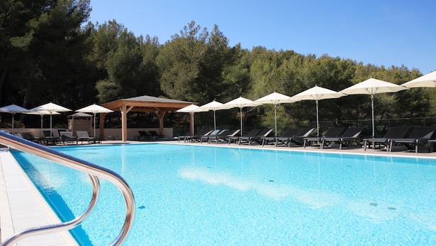 Piscina com espreguiçadeiras e guarda-sóis, rodeada por árvores.