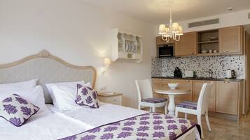 Habitación de hotel con cama, una pequeña mesa de comedor, sillas, una kitchenette y una lámpara en el techo.