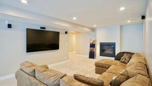 Una sala de estar moderna con un televisor de pantalla plana grande montado en la pared, una chimenea y una zona de estar acogedora con un sofá y un reposapiés.