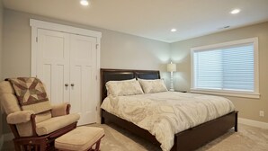 Un dormitorio con una cama, una silla, una lámpara, una ventana con persianas y una puerta.