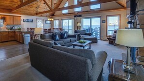 A spacious living area with a high ceiling and wooden beams, a large sofa, a coffee table, and a fireplace. - Serenity Place: 5 bedroom lake home, hot tub, pool table/game room (Penn Yan)