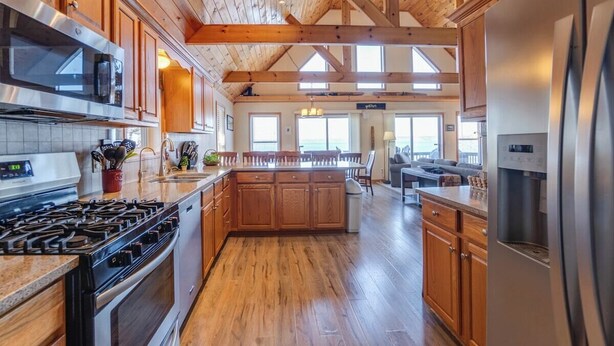 A spacious kitchen with wooden cabinets, a stainless steel refrigerator, and a large island. - Serenity Place: 5 bedroom lake home, hot tub, pool table/game room (Penn Yan)