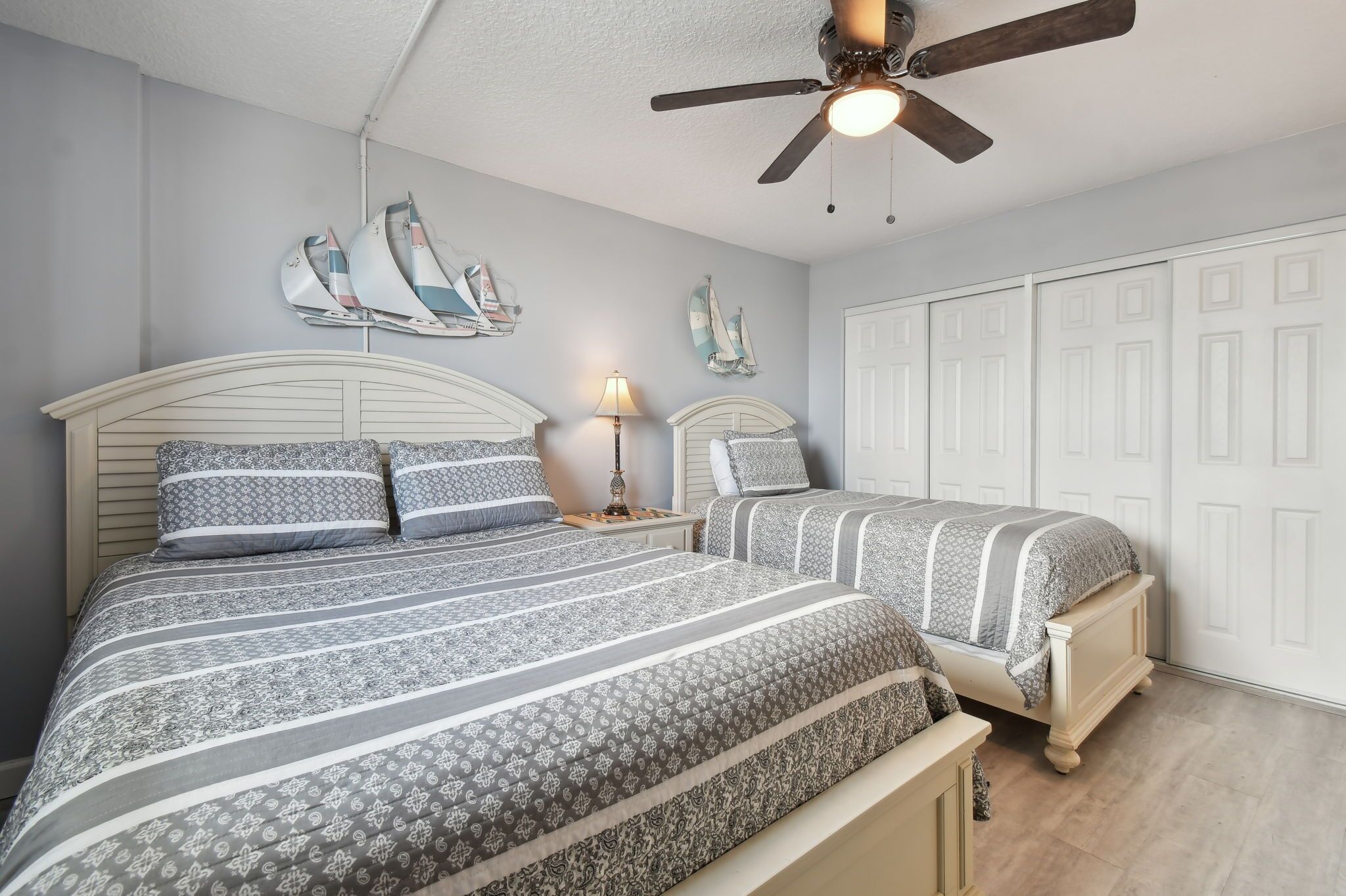 A bedroom with two beds, a ceiling fan, and a wardrobe.