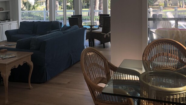 A spacious living area with a large window, a ceiling fan, and a dining table with wicker chairs. - Sea Pines Home with Sparkling Heated Pool-Hole #2 Harbour Town Golf Links-Grill (Hilton Head Island)