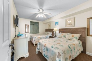 A hotel room with two beds, a desk, a ceiling fan, and a television. - Amazing Oceanfront Condo, Outdoor Pool and Hot Tub | Crescent Keyes - 1006 (North Myrtle Beach)