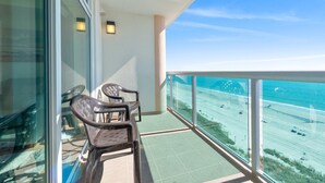 A balcony with two chairs and a table, overlooking a beach and a clear sky. - Amazing Oceanfront Condo, Outdoor Pool and Hot Tub | Crescent Keyes - 1006 (North Myrtle Beach)