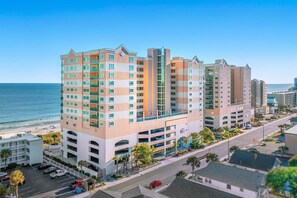 A multi-story hotel with a modern design, featuring balconies, a parking garage, and a view of the beach. - Amazing Oceanfront Condo, Outdoor Pool and Hot Tub | Crescent Keyes - 1006 (North Myrtle Beach)