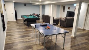 A room with a pool table, a ping pong table, and a sofa. - 6BR Family Retreat - Heated Pool & Game Room - Near Lake George & Saratoga (Corinth)